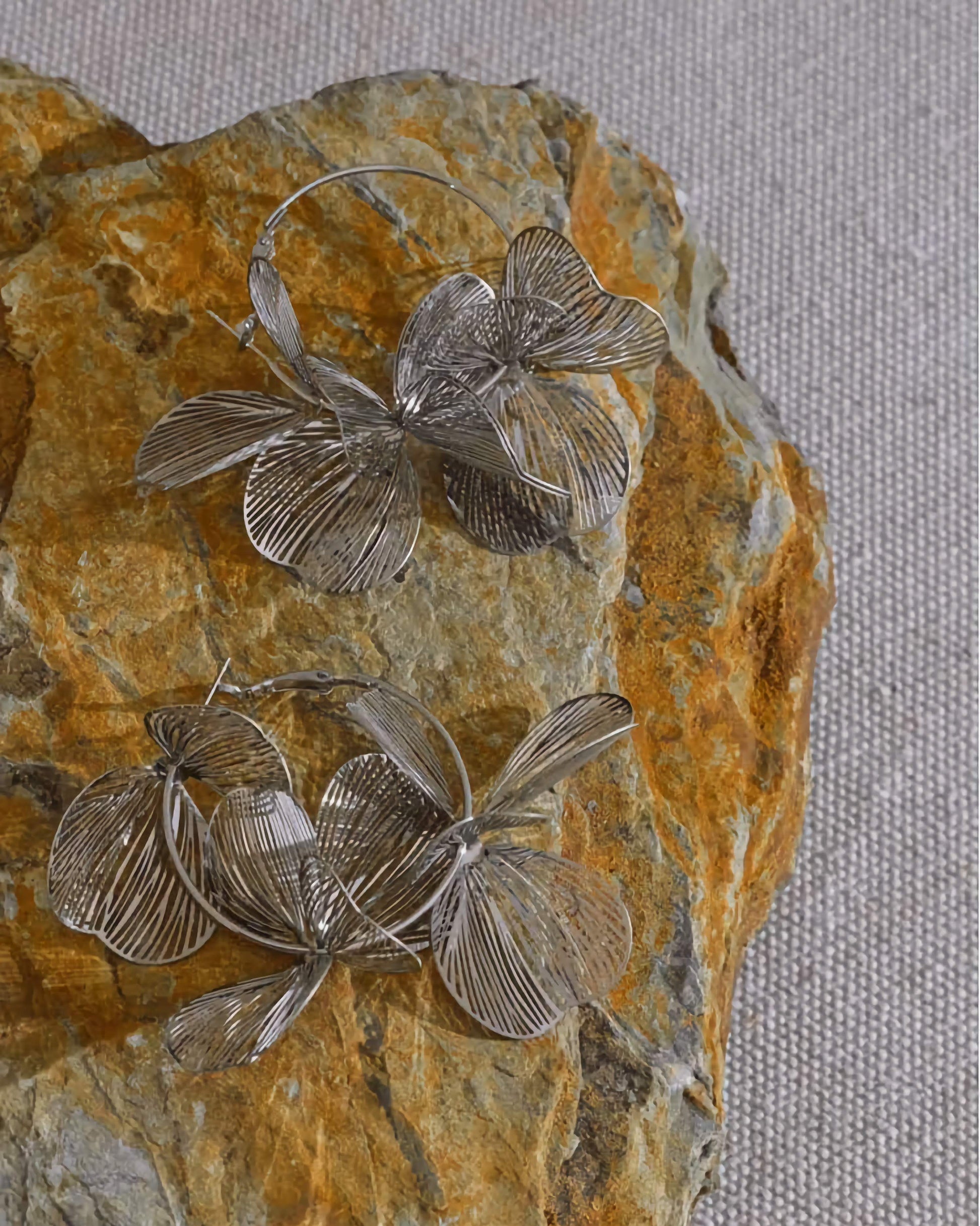 Silver Flower Motif Hoop Earrings displayed over rock