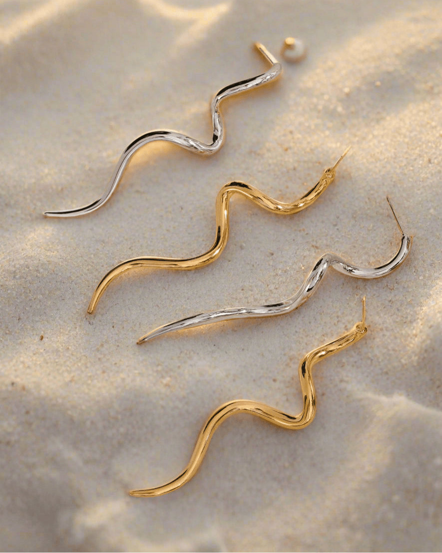 Gold and Silver Abstract Serpentine Drop Earrings, displayed on sand