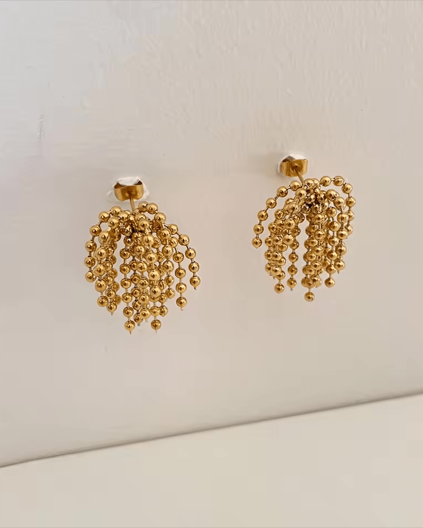 Gold Cascading Ball Chain Drop Earrings dangling on wall display