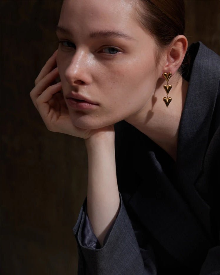 Elegant young woman models Gold Heart Charms Dangle Earrings, side